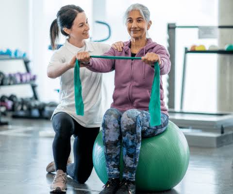 Physiotherapist supervising a patient using a resistance band while seated on an exercise ball